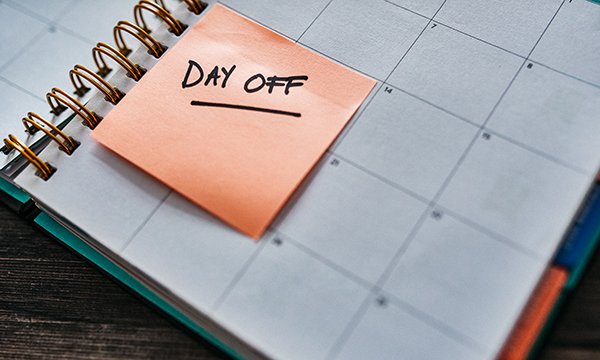 Desk calendar with a sticky note marking a day off. Annual leave will be paid in a new way for nurses or other employees who work irregular hours