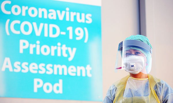 A woman stands next to a sign about coronavirus wearing PPE, including a face mask. Picture: Shutterstock
