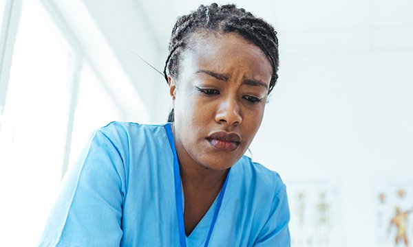 A nurse in scrubs is frowning and hunching her shoulders in a sign of distress
