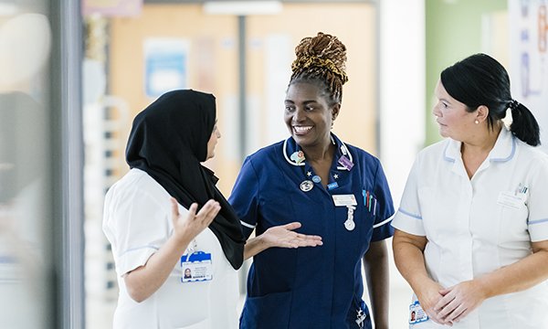 Three nurses stand talking and appearing happy to be working together