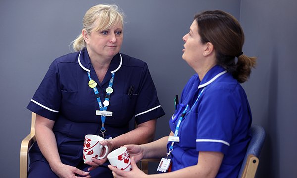 A nurse manager listens to a stressed nurse while they chat and drink a mug of tea