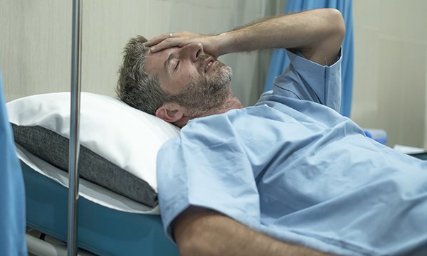A man lying on an emergency department bed holds his head in pain