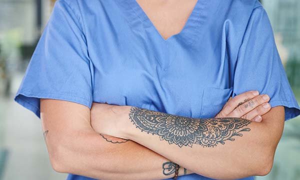 Close-up of nurse with tattooed arms crossed