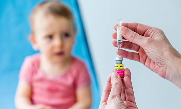Nurse's hands seen preparing vaccine for child. MMR uptake is down, and measles cases in UK going up