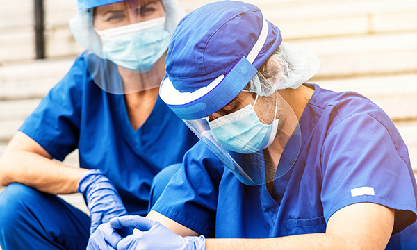 Two medics in personal protective equipment, one looking concerned as the other appears upset