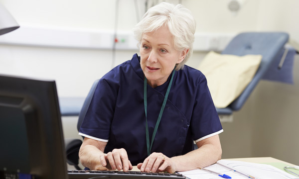 Picture shows older woman in medic's uniform looking at computer screen
