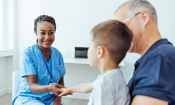 A nurse holds hands with a child who is sitting on their father’s lap