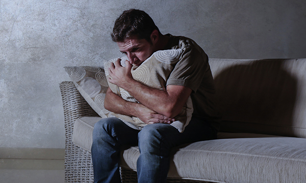 An isolated man hugs a pillow on a sofa. Mental healthcare and distress: Lack of nursing experience and confidence to manage distress can lead to a dependence on restraint, seclusion and/or enhanced observations