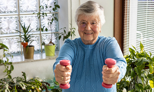 An older woman holding weights in each hand. Exercise should include weight-bearing and muscle-strengthening activities.