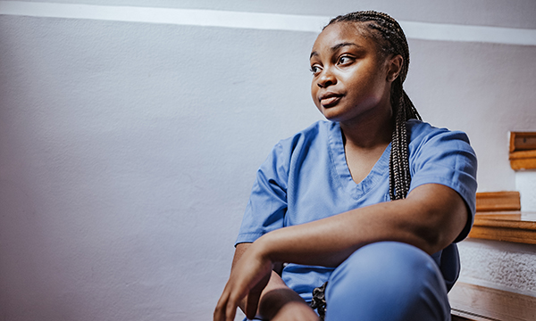 A nurse with a contemplative expression sits looking into the distance