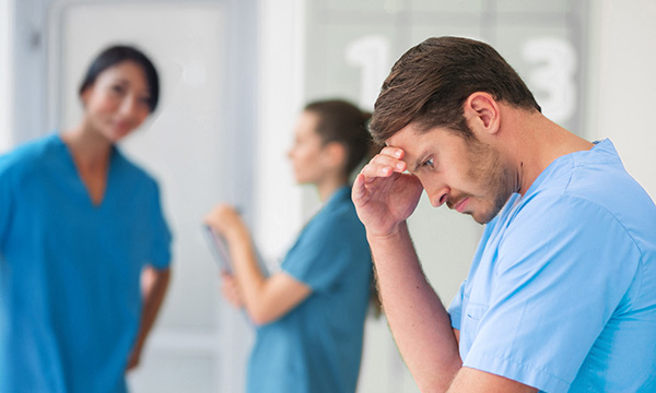 ex discrimination against men in nursing: male staff member appears under stress, female colleagues in the background