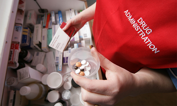 Drug calculations in nursing: nurse wearing red tabard arranges medicines on a drugs trolley