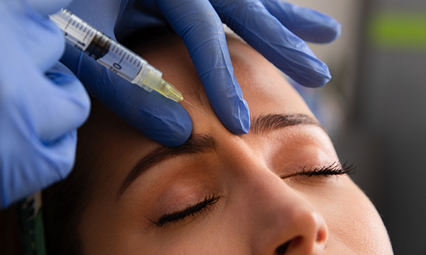 A woman receiving a Botox injection by someone wearing disposable gloves
