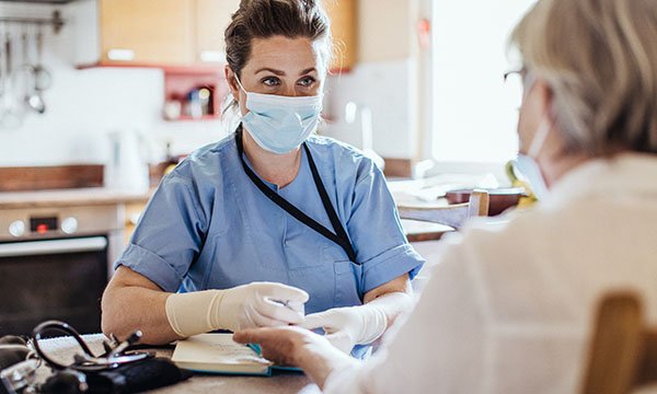 A healthcare worker wearing mask and protective gloves examines a patient