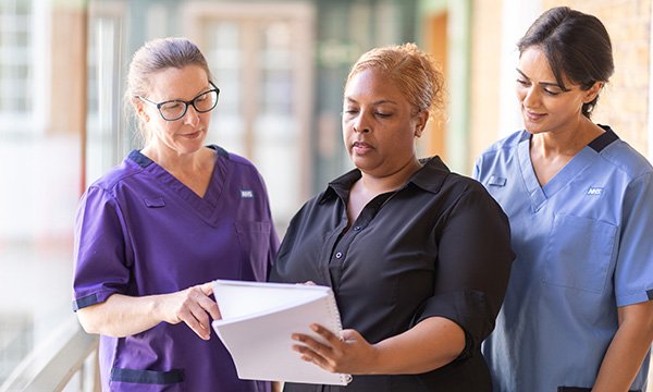 A senior nurse consults her notes and speaks to two other nurses in her team