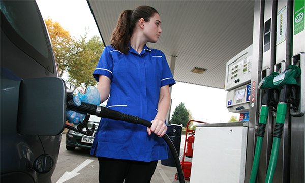 A nurse in uniform fills up her car at a petrol pump