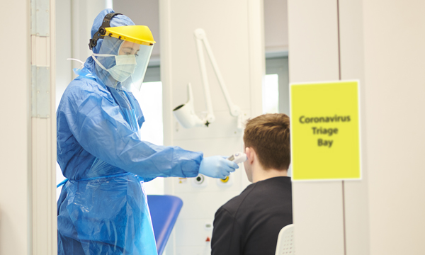 A healthcare worker in full PPE conducting a COVID-19 test in a coronavirus triage bay