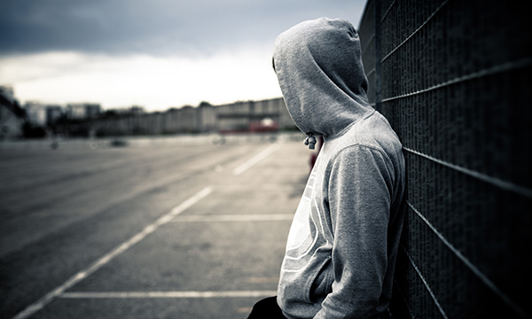Hooded young person with back to the wall looking out on a street