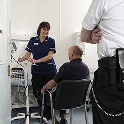 A nurse providing care to an individual in prison, with a guard present