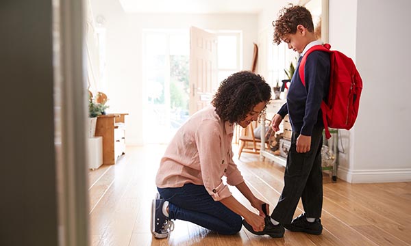 A woman bends down to tie her child’s shoelaces as he gets ready to go to school. Band 5 roles can offer nurses greater flexibility with home and caring responsibilities