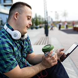 A young man with learning disabilities sits and looks at a tablet computer with headphones around his neck: making a music playlist can help someone celebrate a close one’s life