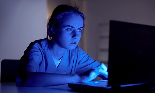 A jaded-looking nurse inputs information on a work laptop late at night. Record-keeping is a common reason nurses are referred to the NMC