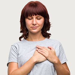 A woman trying to reduce anxiety by following a breathing exercise that starts with placing your hand on your heart and breathing deeply