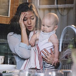 Picture shows strained mother at the kitchen sink with baby