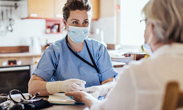 A healthcare worker wearing a mask and protective gloves talks to a female patient