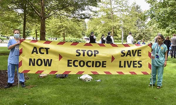 Extinction Rebellion protest at Shell Tower, London: nurses hold a banner saying: 'Act now, stop Ecocide, save lives' which mimics the COVID-19 advice posters by the government