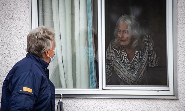 Person with mask looking at care home resident through window
