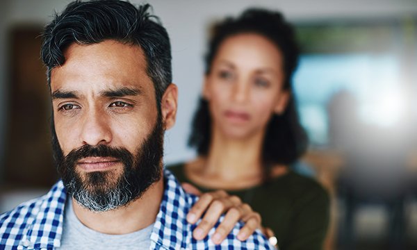 Picture shows worried man with woman standing behind with her hand on his shoulder
