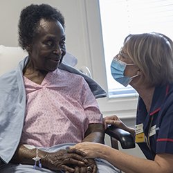 A masked nurse communicates respectfully with an older woman patient
