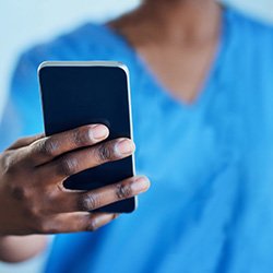A nurse in uniform holding a smartphone. Nurses are being alerted to vaccination availability via app messages and social media