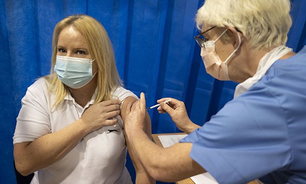 A nurse administers the COVID-19 vaccine to another another member of the healthcare workforce