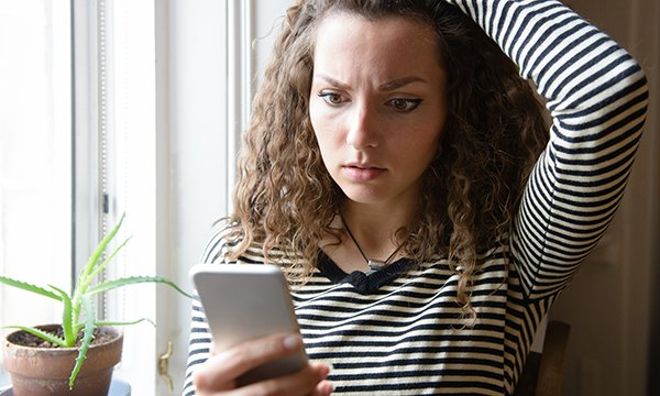 Picture shows a perplexed young woman looking at her phone