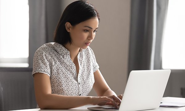 Picture shows a woman of Asian ethnicity typing on a laptop