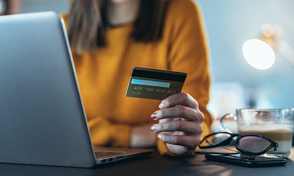 woman sits at laptop, with payment card in hand