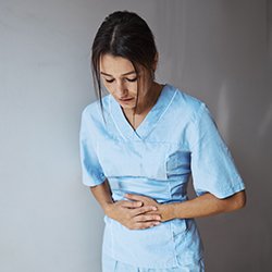 young nurse holds her abdomen as if in pain
