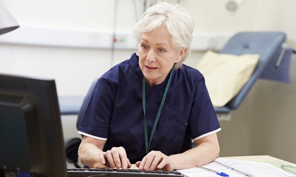 Picture shows older woman in medic's uniform looking at computer screen