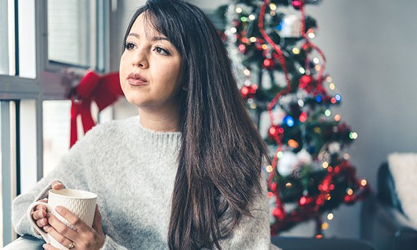 Woman gazing out the window with a Christmas tree behind her