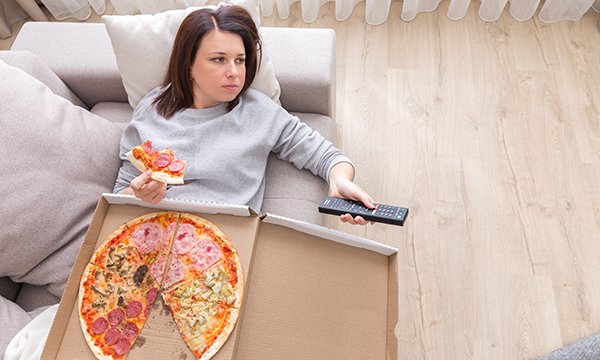 A nurse lying on a sofa after a shift, eating pizza from a box