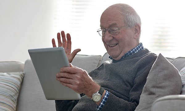 Older man taking a video call via iPad. A Nursing Older People evidence & practice article evaluates the benefits and challenges of video consultations for carers of people living with dementia