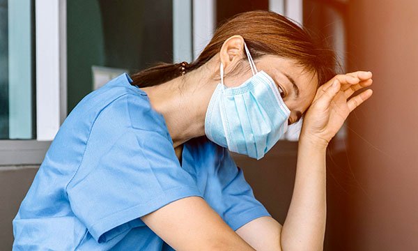 Exhausted-looking nurse sits leaning her head against a wall