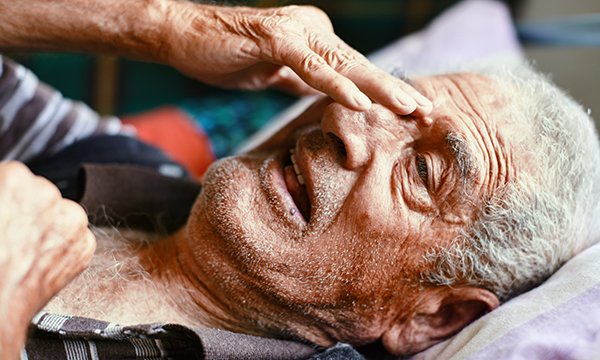 Photo of a man lying in bed holding his head in pain