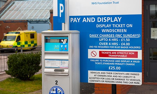 A hospital car park pay meter with a sign detailing parking charges