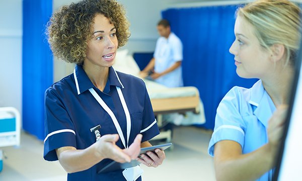 More experienced nurse talks to newly qualified nurse on a ward