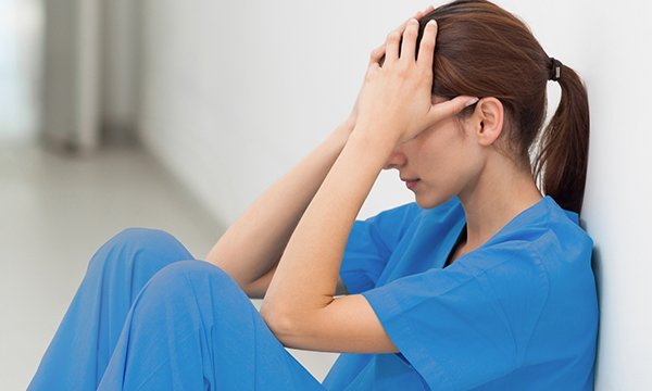A nurse in scrubs sitting on the floor looking exhausted