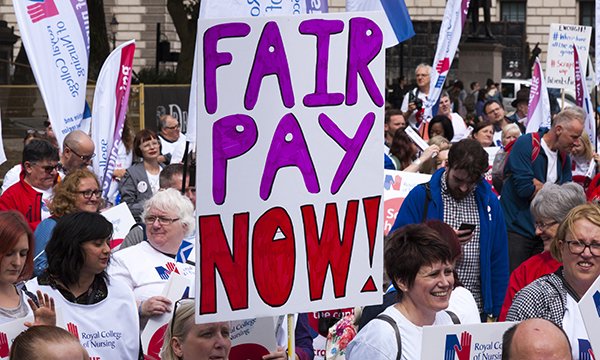 Photo of a crowd of nurses marching with banners saying Fair Pay Now