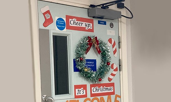 Photo of a door on a hospital ward decorated with a wreath and tinsel and the words 'Cheer up, it's Christmas'